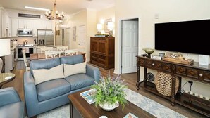 A modern living room with a blue sofa, a coffee table, a TV, and a kitchen in the background.