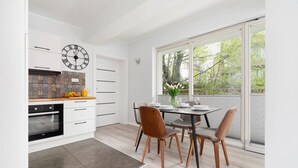 A modern kitchen with white cabinetry, a black oven, and a patterned backsplash. There is a dining area with a table set for four, featuring wooden chairs and a vase of flowers.