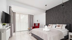 A modern hotel room with a large bed, a flat-screen TV, a red chair, and a view of the outdoors.