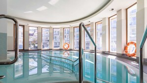 An indoor swimming pool with clear glass walls, metal railings, and lifebuoys.