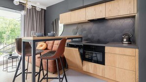 Una cocina moderna con armarios de madera, un lavavajillas negro y una zona de comedor con un sofá marrón y sillas de metal.