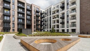 Un edificio residencial de varios pisos con balcones, un patio ajardinado con macetas de madera y un camino pavimentado.