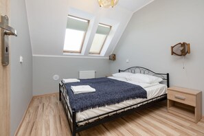 Une chambre avec un plafond en pente, des fenêtres de toit, un lit recouvert d’une couverture bleue, une table de chevet et une commode en bois.