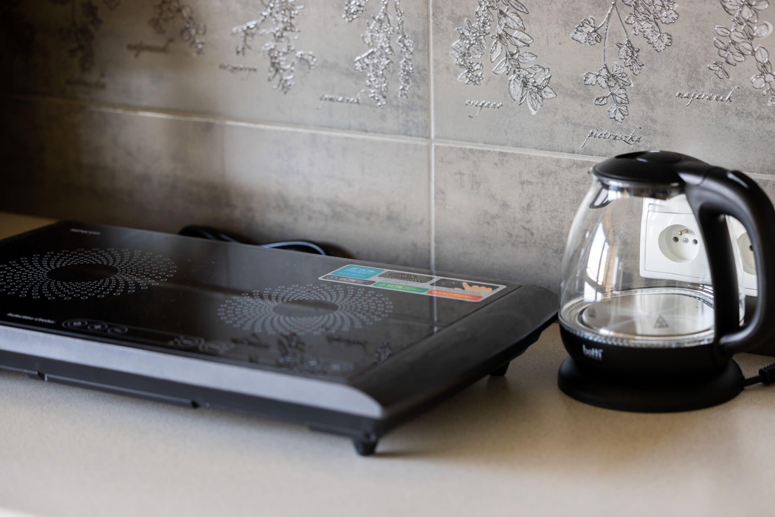 Une cuisine avec une plaque de cuisson à induction noire et une bouilloire en verre posée sur le plan de travail.
