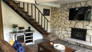 A living room with a stone wall, a fireplace, a staircase, and a mounted TV.