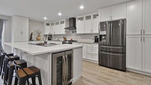 A modern kitchen with white cabinetry, a stainless steel refrigerator, and a central island with bar stools.