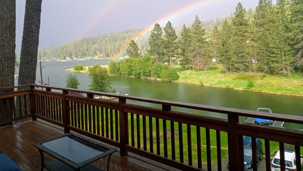 A wooden deck with a view of a river, trees, and a rainbow.