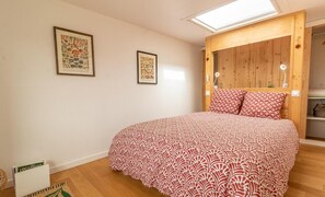Een slaapkamer met een bed, een houten hoofdeinde, twee ingelijste botanische prints en een dakraam.