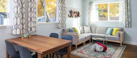 Una sala de estar moderna con una mesa de comedor de madera, un sofá gris y cortinas estampadas.