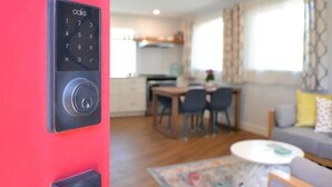Un sistema de cierre con teclado en una pared roja, un comedor con sillas y una mesa, y una sala de estar con un sofá y una mesita de centro.