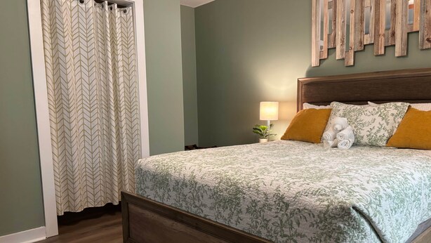 A bedroom with a bed, a nightstand with a lamp, a wooden headboard, and a wall-mounted mirror. - Woodward Villa A (Dahlonega)