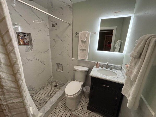 Un baño con ducha, inodoro, lavabo y espejo.
