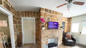 A living room with a stone fireplace, a television, a ceiling fan, and a black leather chair. - Woodward Villa A (Dahlonega)