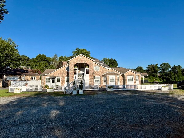 A two-story stone building with a central archway, white picket fence, and a gravel driveway.