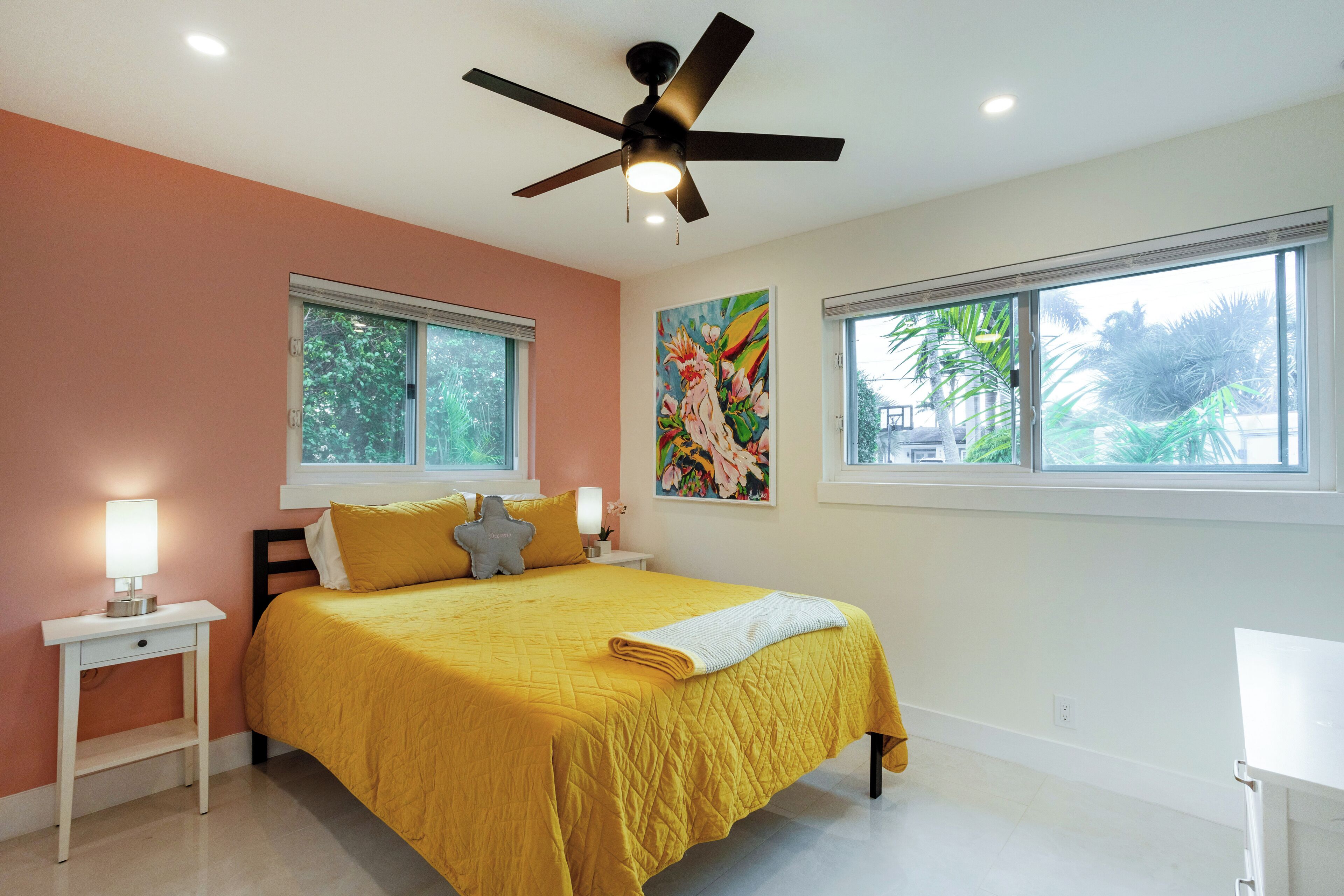 A bedroom with a bed, two bedside tables, a ceiling fan, and two windows.
