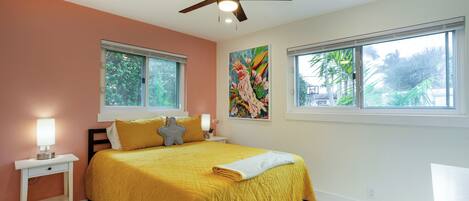 A bedroom with a bed, two bedside tables, a ceiling fan, and two windows.