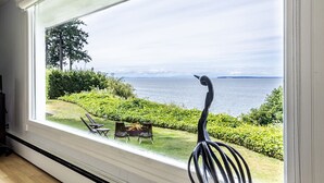 A room with a large window overlooking a garden and a body of water. - Peaceful Beachfront Getaway with Sweeping Water Views (Blaine)