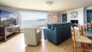 A living room with a large TV, a sofa, a coffee table, and a view of the sea. - Peaceful Beachfront Getaway with Sweeping Water Views (Blaine)