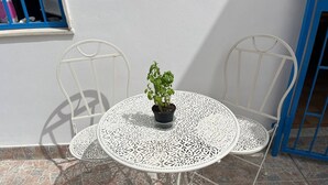 Una mesa redonda con elaborada filigrana de metal blanco, dos sillas de metal blanco y una planta en maceta sobre la mesa.