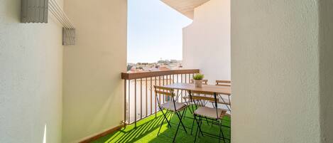 A balcony with a wooden table and chairs, a small potted plant, and artificial green grass flooring.