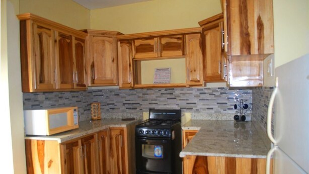A kitchen with wooden cabinets, a stove, a microwave, and a refrigerator. - A cozy home in a quiet residential community  minutes from Town Central (Montego Bay)