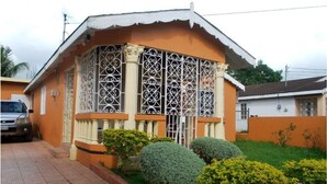 A house with a balcony, a car parked in front, and a well-maintained garden. - A cozy home in a quiet residential community  minutes from Town Central (Montego Bay)