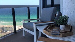 A balcony with a view of the ocean, a white chair with a cushion, a small table with a tray, and a potted plant. - PENTHOUSE -16TH FLOOR with FREE BEACH SERVICE.  AMAZING VIEW!! (Miramar Beach)