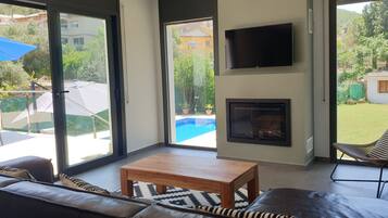 Een moderne woonkamer met een open haard, een televisie en uitzicht op een zwembad en tuin.