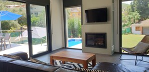 Un salon moderne doté d’une cheminée, d’un téléviseur et offrant une vue sur une piscine et un jardin.