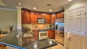 A kitchen with granite countertops, stainless steel appliances, wooden cabinets, and a white door. - [NEW] Luxe Resort Villa w/Golf Course Views Near Disney (Reunion)