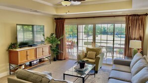A living room with a television, sofa, armchair, and a large window with curtains. - [NEW] Luxe Resort Villa w/Golf Course Views Near Disney (Reunion)