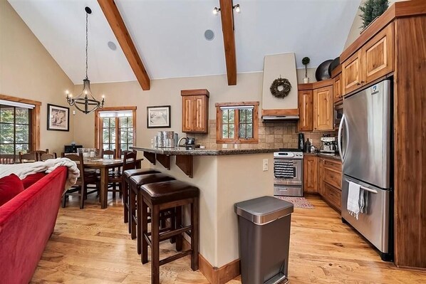 A spacious kitchen with wooden cabinets, a stainless steel refrigerator, and a dining area with a red sofa and wooden stools.