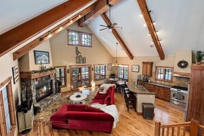A spacious loft with a high ceiling, exposed wooden beams, a fireplace, a red sofa, a dining area, and a kitchen with wooden cabinets.