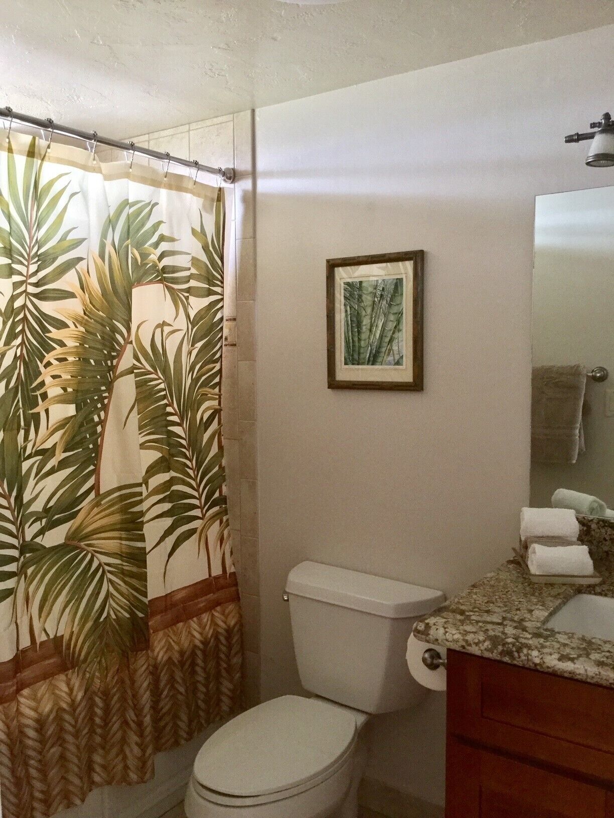 A bathroom with a toilet, a sink, and a shower curtain with a tropical leaf pattern.
