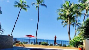 A swimming pool with a view of the ocean, surrounded by palm trees and a red umbrella. - AMAZING HOTEL ZONED BEACH FRONT CONDO ON SUGAR BEACH.  RESERVE WITH CONFIDENCE! (Kihei)