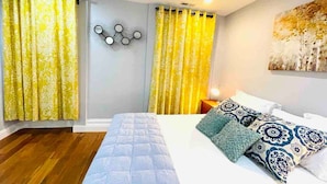 Un dormitorio con cama, cortinas amarillas, un reloj de pared y un cuadro.