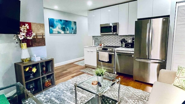 Una cocina moderna con electrodomésticos de acero inoxidable, un comedor con una mesa de centro de vidrio y una sala de estar con sofá.