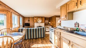 A cozy cabin-style kitchen with wooden cabinets, a dining area with a table and chairs, a striped sofa, and a stove.
