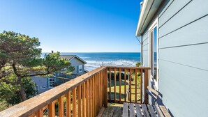 A wooden deck with a view of the ocean and a house with light blue siding.