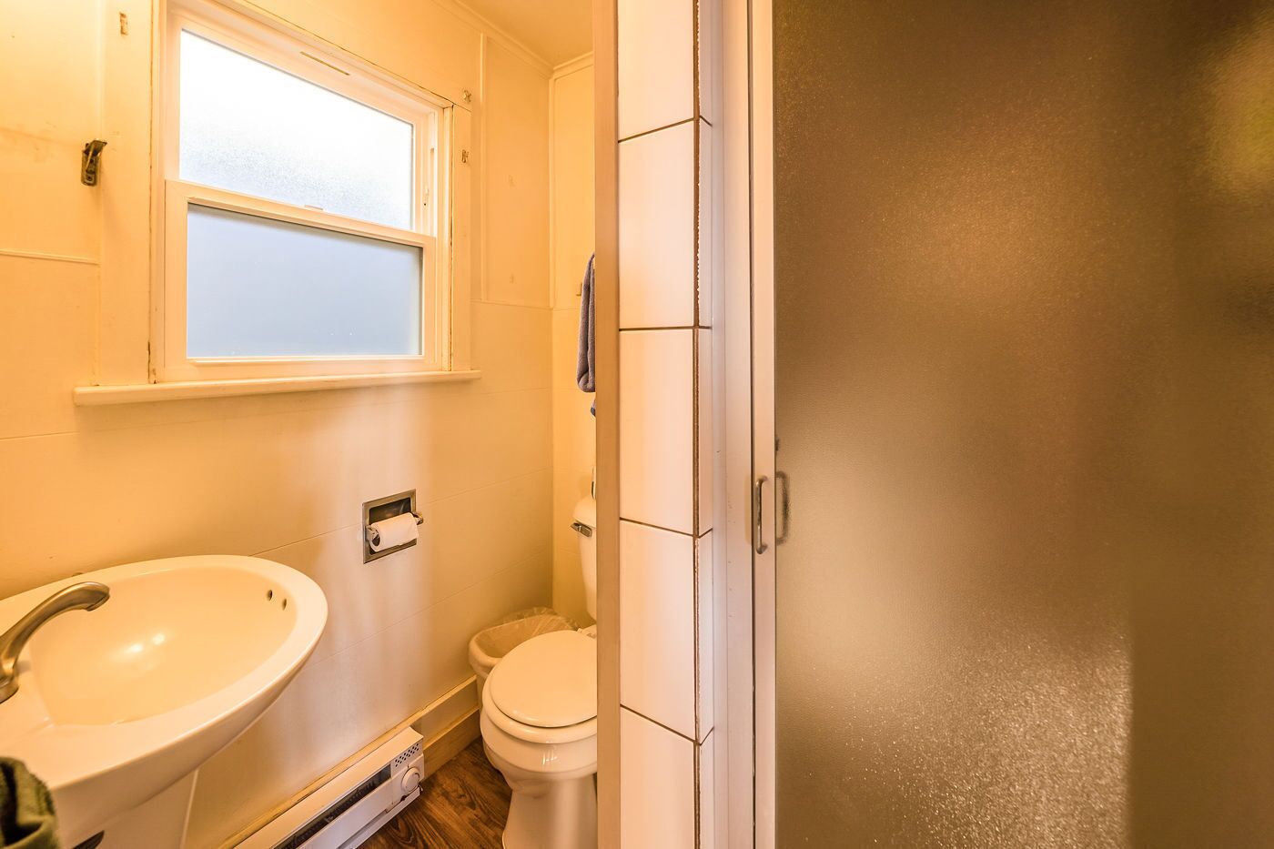 A small bathroom with a white sink, toilet, and window.