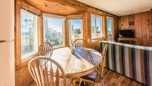 A wooden cabin with a dining table and chairs, a television, and large windows.