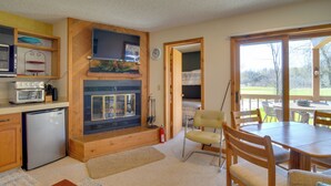 A kitchen with a built-in oven, a refrigerator, and a television above the oven. There is a dining area with a table and chairs. - Schuss Mountain Resort Condo: Steps to Golf! (Mancelona)