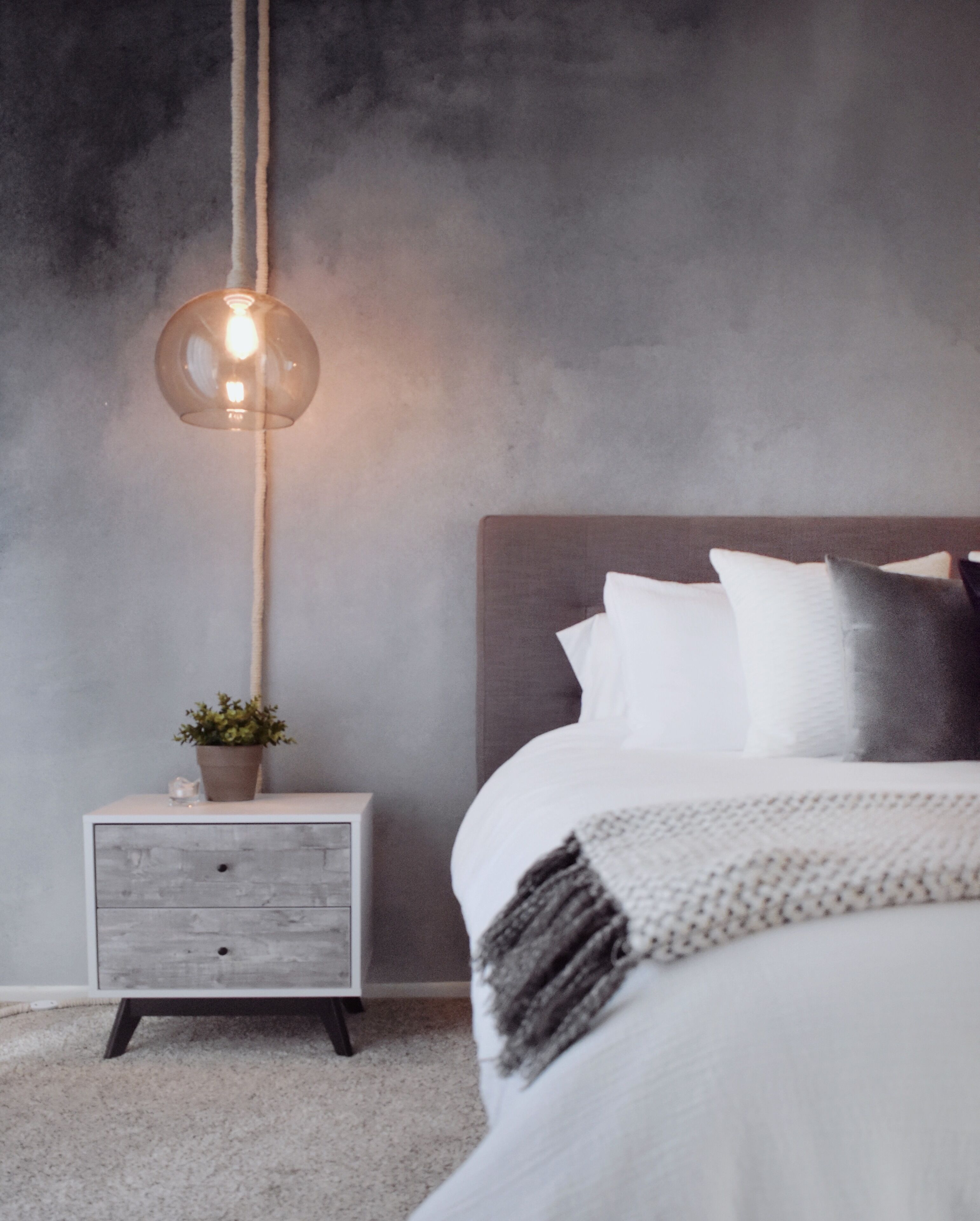 A bedroom with a bed, bedside table, lamp, and a wall with a textured finish.