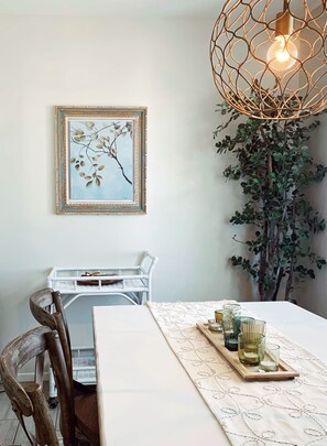 A dining area with a table set for two, featuring a framed botanical print and a unique pendant light.
