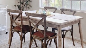 Un coin repas avec une table blanche et quatre chaises en bois, un luminaire suspendu et une grande fenêtre donnant sur des arbres.