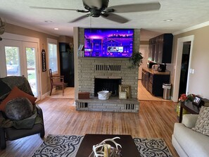 A living room with a fireplace, a television mounted above it, and a ceiling fan. - Lake View Home (Mountain Home)