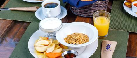 A breakfast table with plates of pancakes, eggs, and toast, a bowl of cereal, a glass of orange juice, and a napkin with a logo.