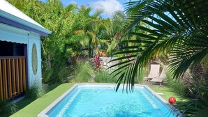 A swimming pool surrounded by lush greenery and a small building with a window.