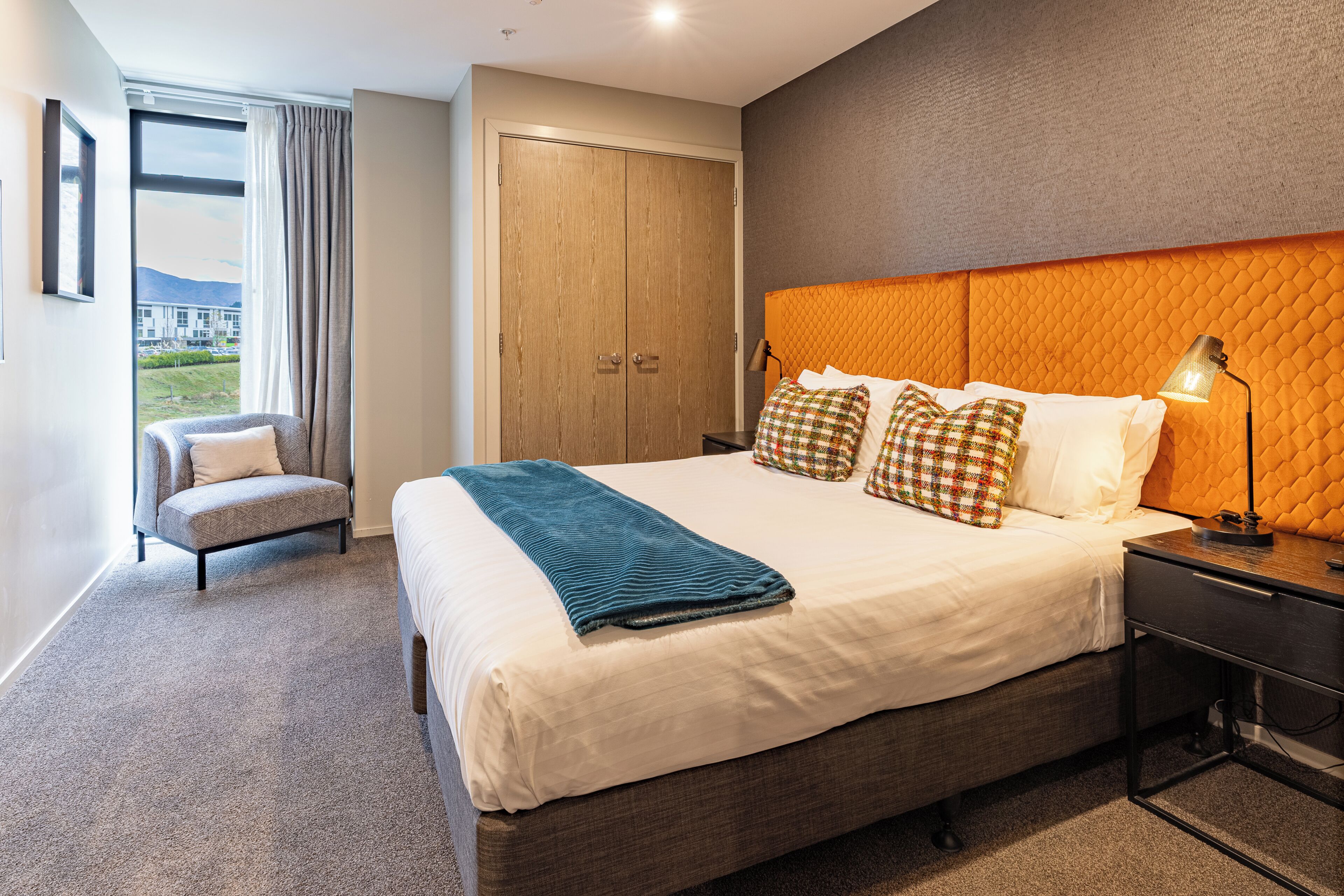 A hotel room with a large bed, a chair, a wardrobe, and a view of the outdoors.