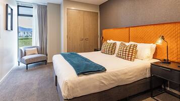 A hotel room with a large bed, a chair, a wardrobe, and a view of the outdoors.